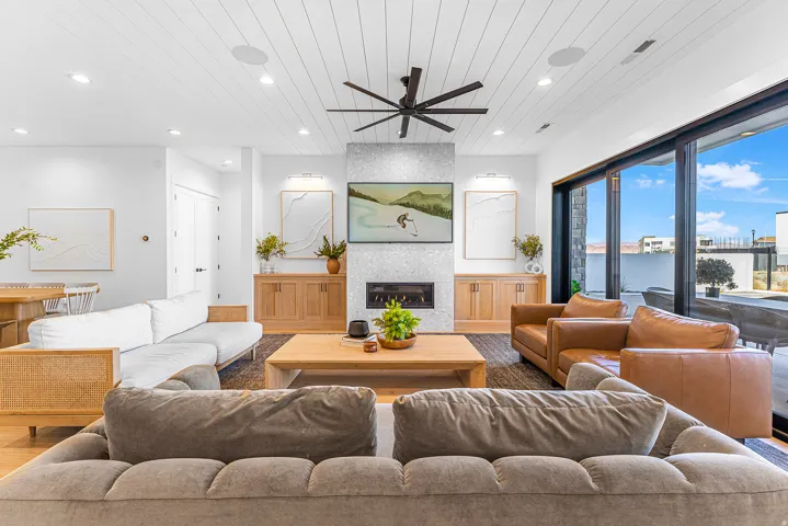Spacious living area featuring a central fireplace with a textured surround, recessed lighting, and a slatted white ceiling
