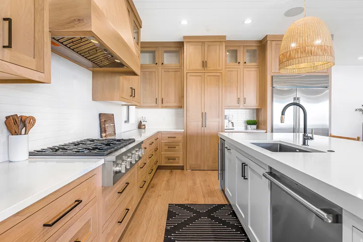 Gourmet kitchen featuring a built-in gas range with a custom hood, stainless steel appliances, extensive light wood cabinetry, white countertops, and a central island with an integrated sink and dishwasher