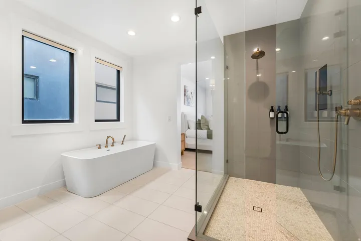 Freestanding soaking tub with floor-mounted brass fixtures, set against a backdrop of two black-framed windows
