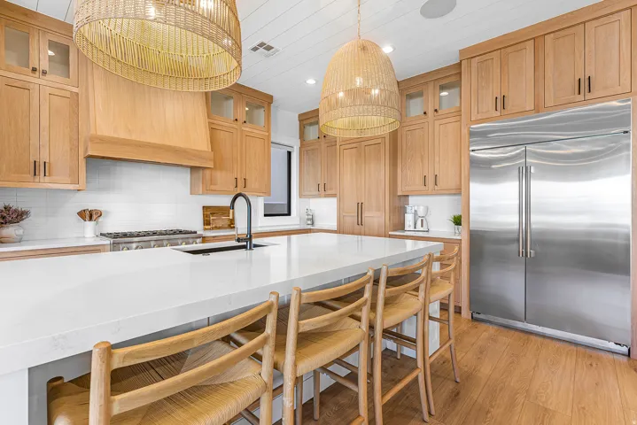 Spacious kitchen featuring a large central island with seating, natural wood cabinetry, stainless steel appliances, white subway tile backsplash, and wood-finish flooring