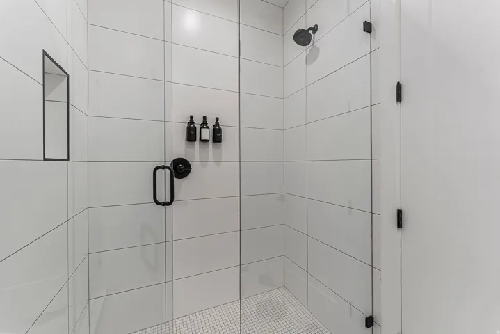 Shower enclosure featuring clear glass panels, matte black hardware, white rectangular wall tiling, a recessed niche, and a mosaic tile floor