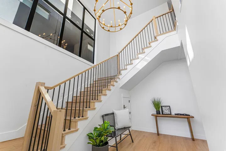 Two-story entry featuring a grand staircase with natural wood treads and handrails, black metal balusters, a large gold-finish chandelier, and a prominent upper window with black framing