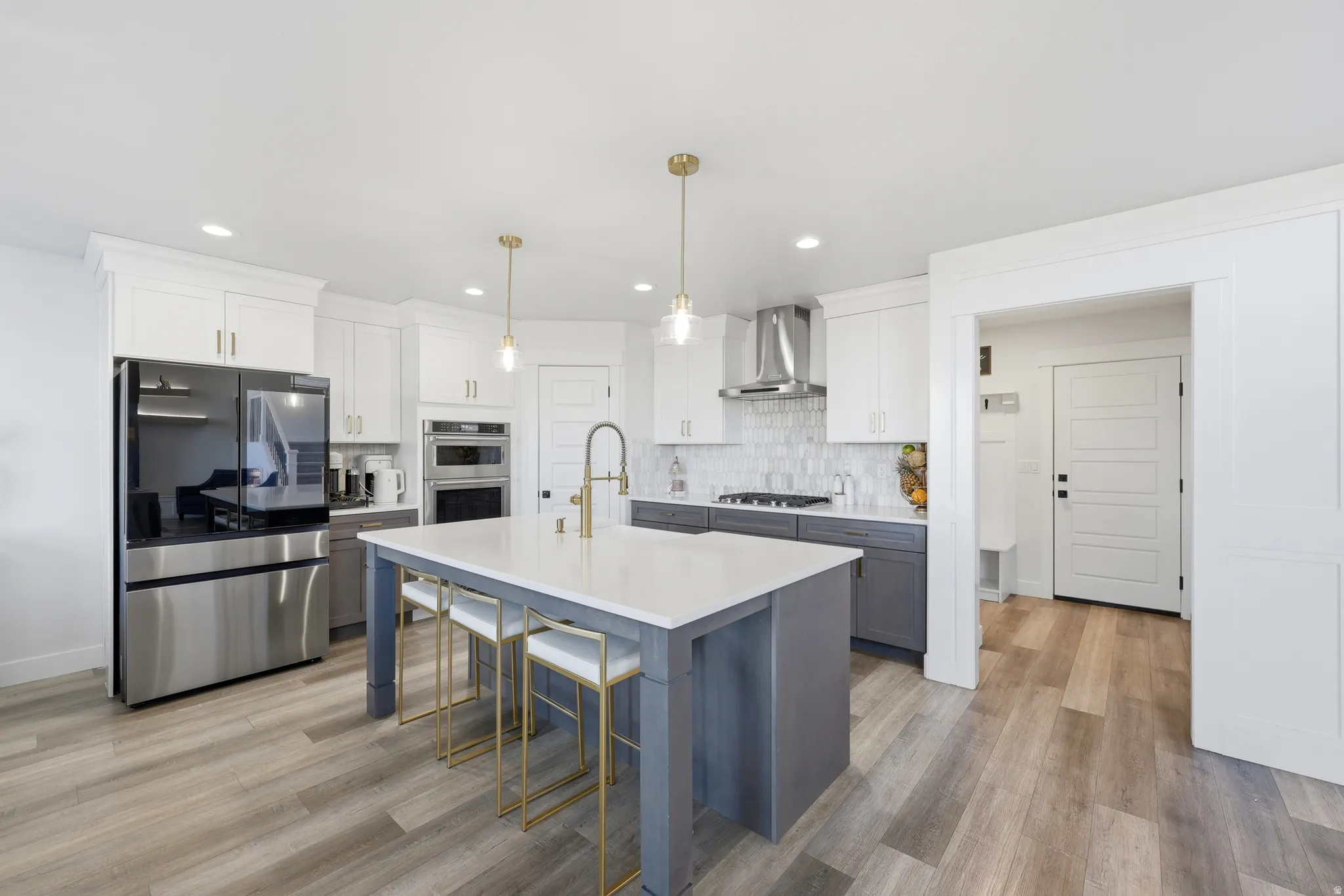 Contemporary kitchen featuring a large center island with a light-toned countertop, two-tone cabinetry, stainless steel appliances, wood-finish flooring, and pendant lighting fixtures