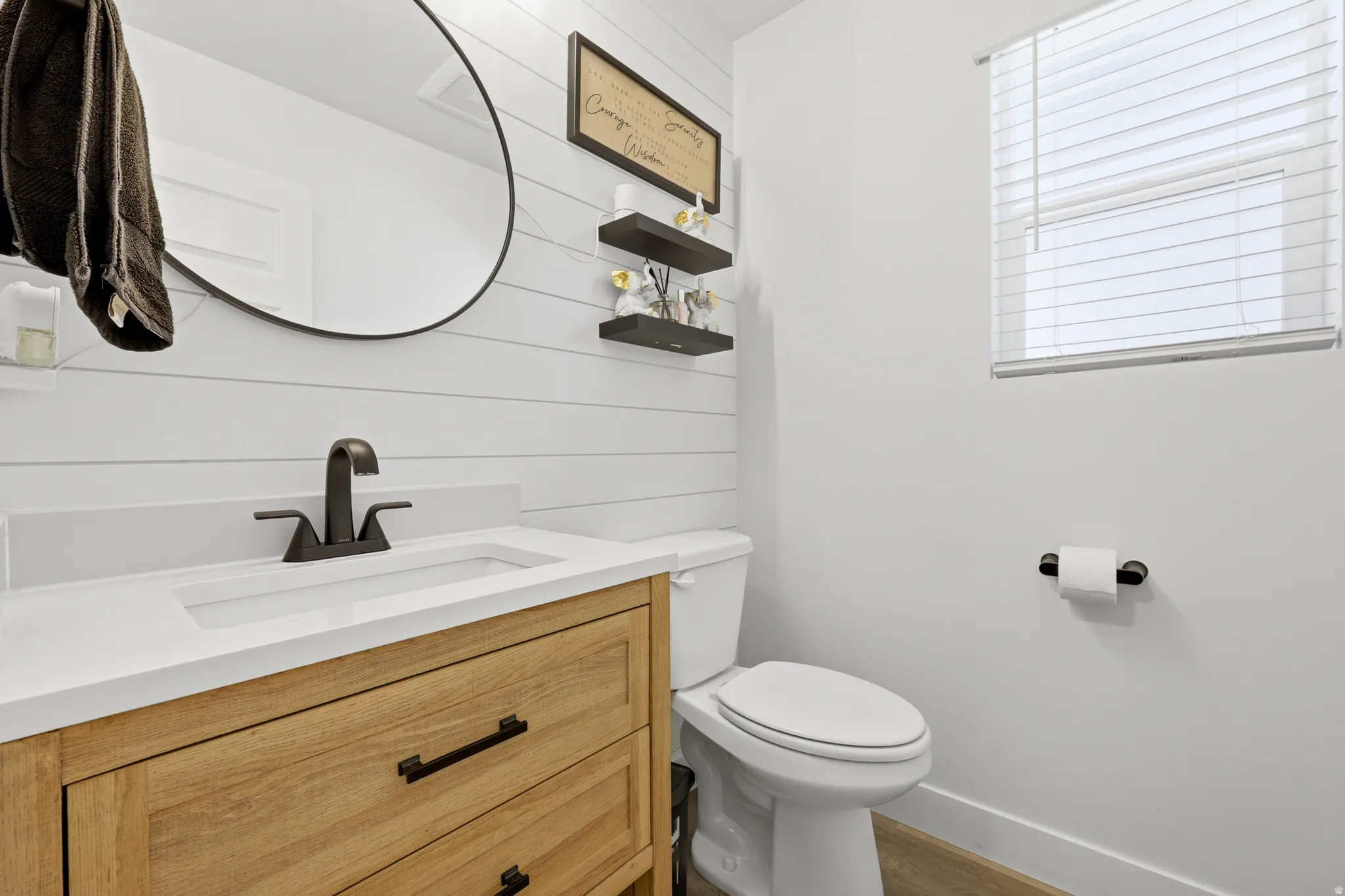 Bathroom featuring a wood-finish vanity with drawer storage, integrated white sink, and dark bronze-tone faucet