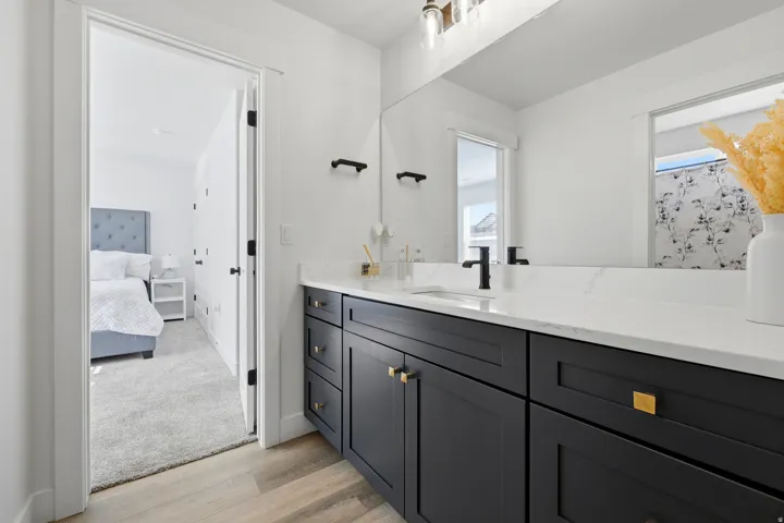 Bathroom vanity featuring dark cabinetry with gold-toned hardware, a white countertop, and a rectangular undermount sink with a matte black faucet