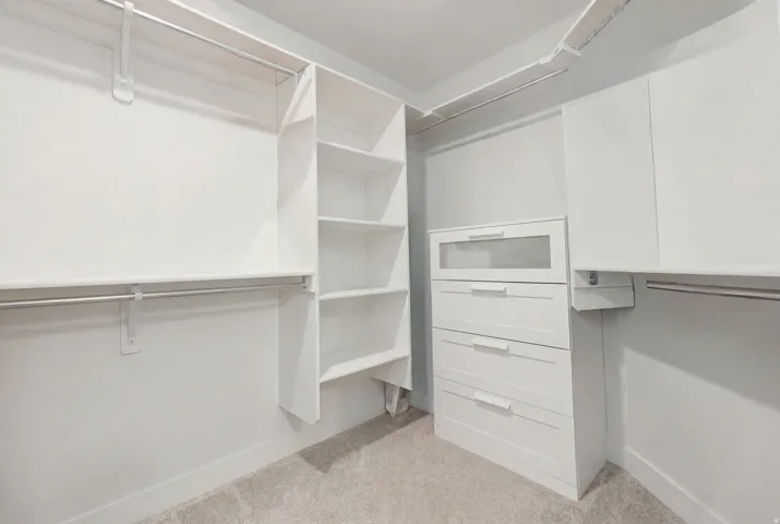 Walk-in closet featuring white built-in shelving, multiple hanging rods, and a white dresser with frosted glass accents