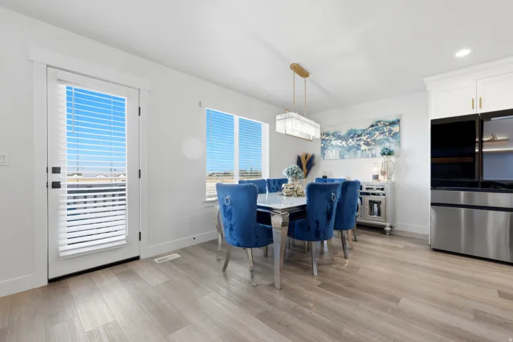 Open-concept dining area featuring light wood-finish flooring, a contemporary rectangular chandelier, and a white paneled exterior door