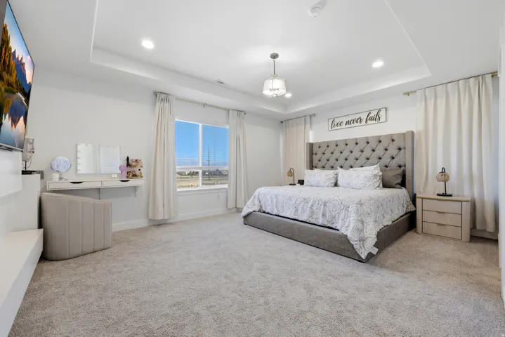 Spacious room featuring tray ceilings with recessed lighting, a large window with horizontal blinds, and neutral carpeting