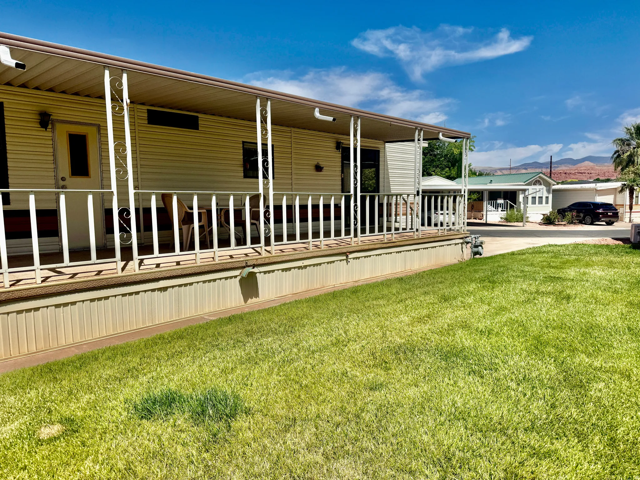 Residential exterior featuring a covered porch with white railing, light-colored siding, and a manicured lawn