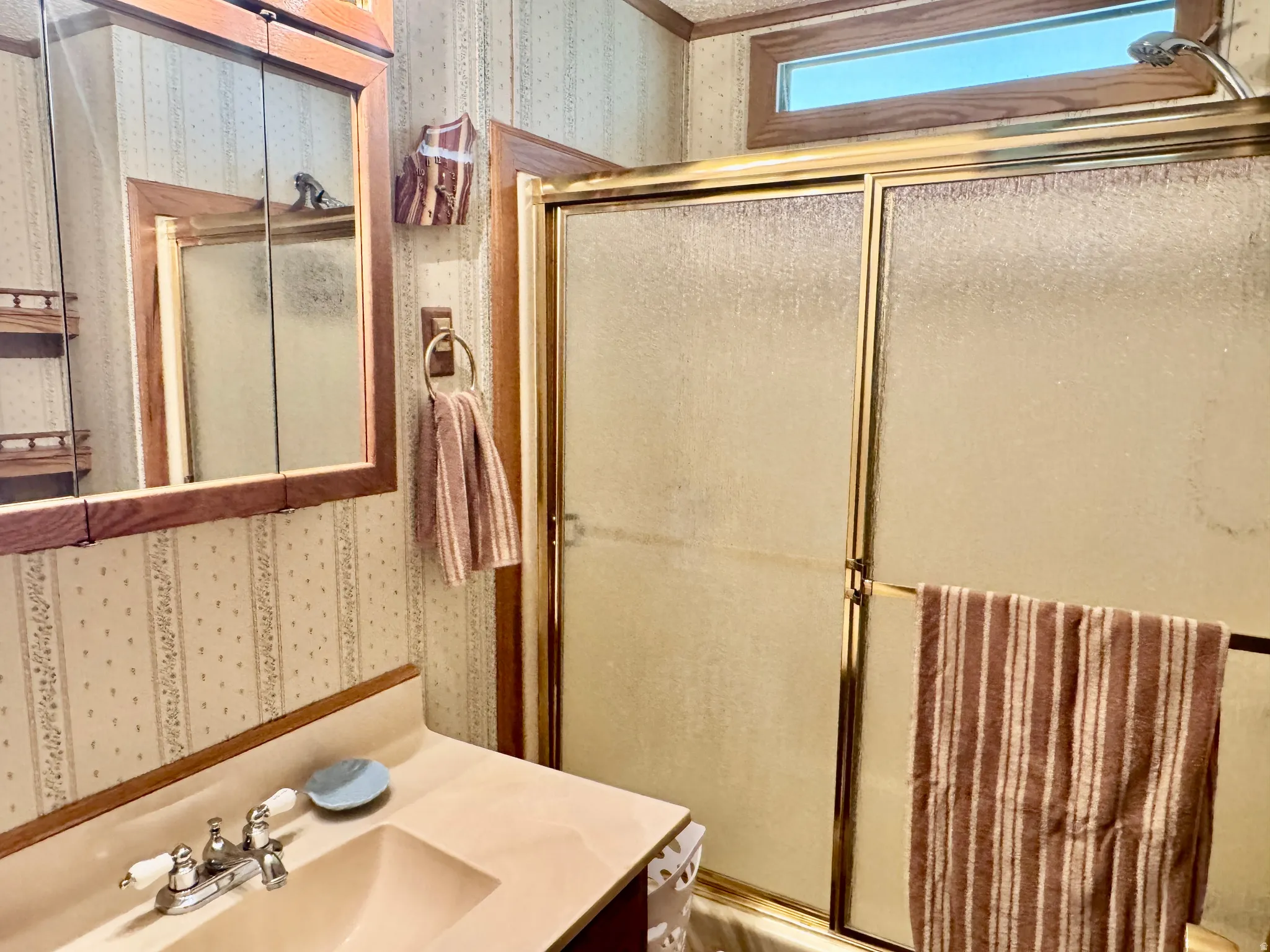 Bathroom featuring a vanity with an integrated sink, a medicine cabinet with a wood-finish frame, and a shower with frosted glass sliding doors and a gold-finish frame