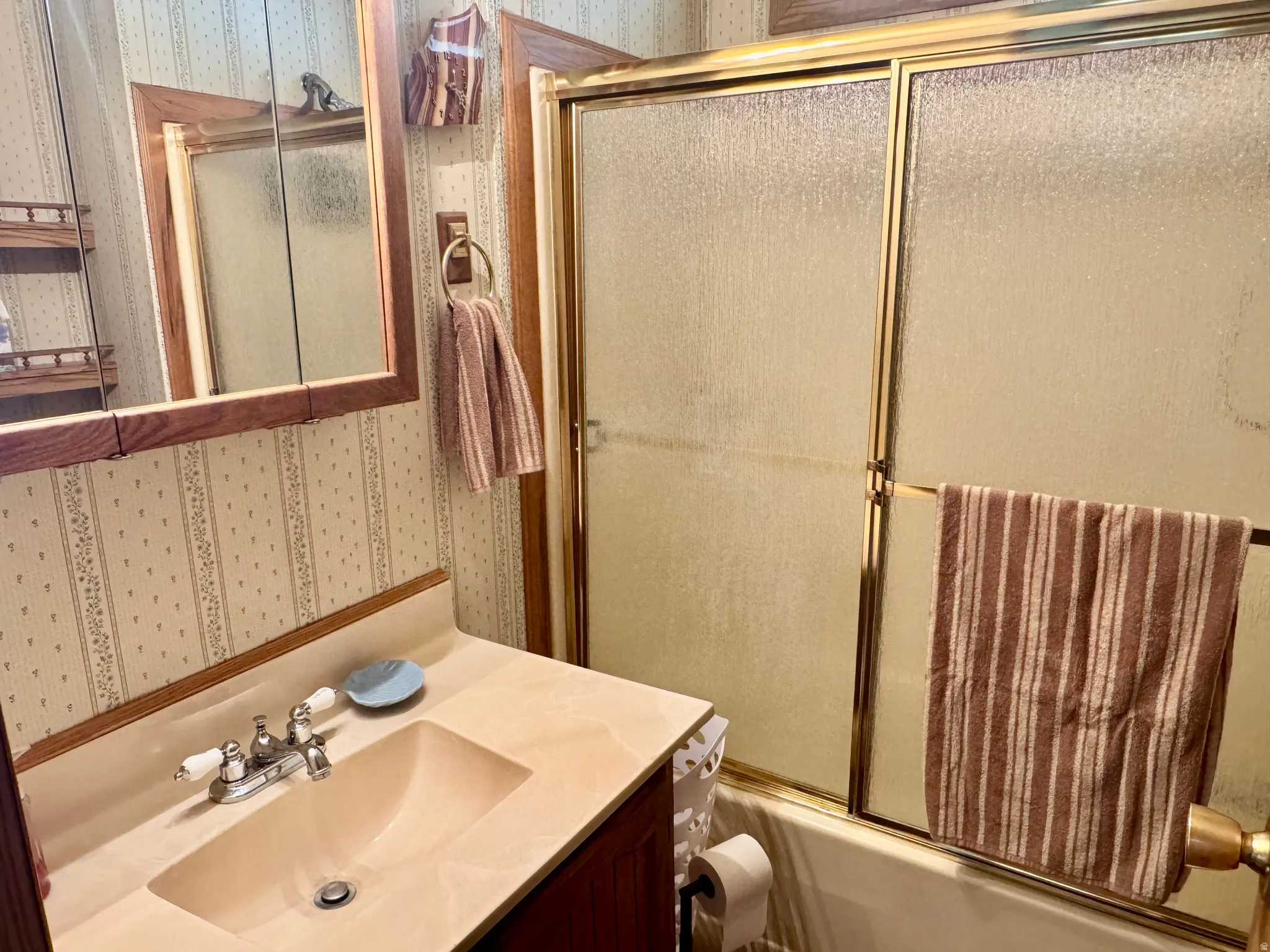 Bathroom featuring a vanity with an integrated sink, polished chrome faucet, wood-finish medicine cabinet, and a bathtub with a framed glass enclosure
