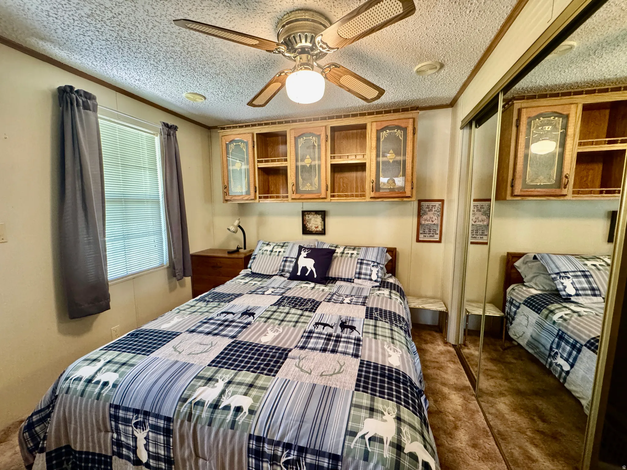 Bedroom featuring a ceiling fan with integrated lighting, wood-finish cabinetry with glass inserts, and mirrored closet doors