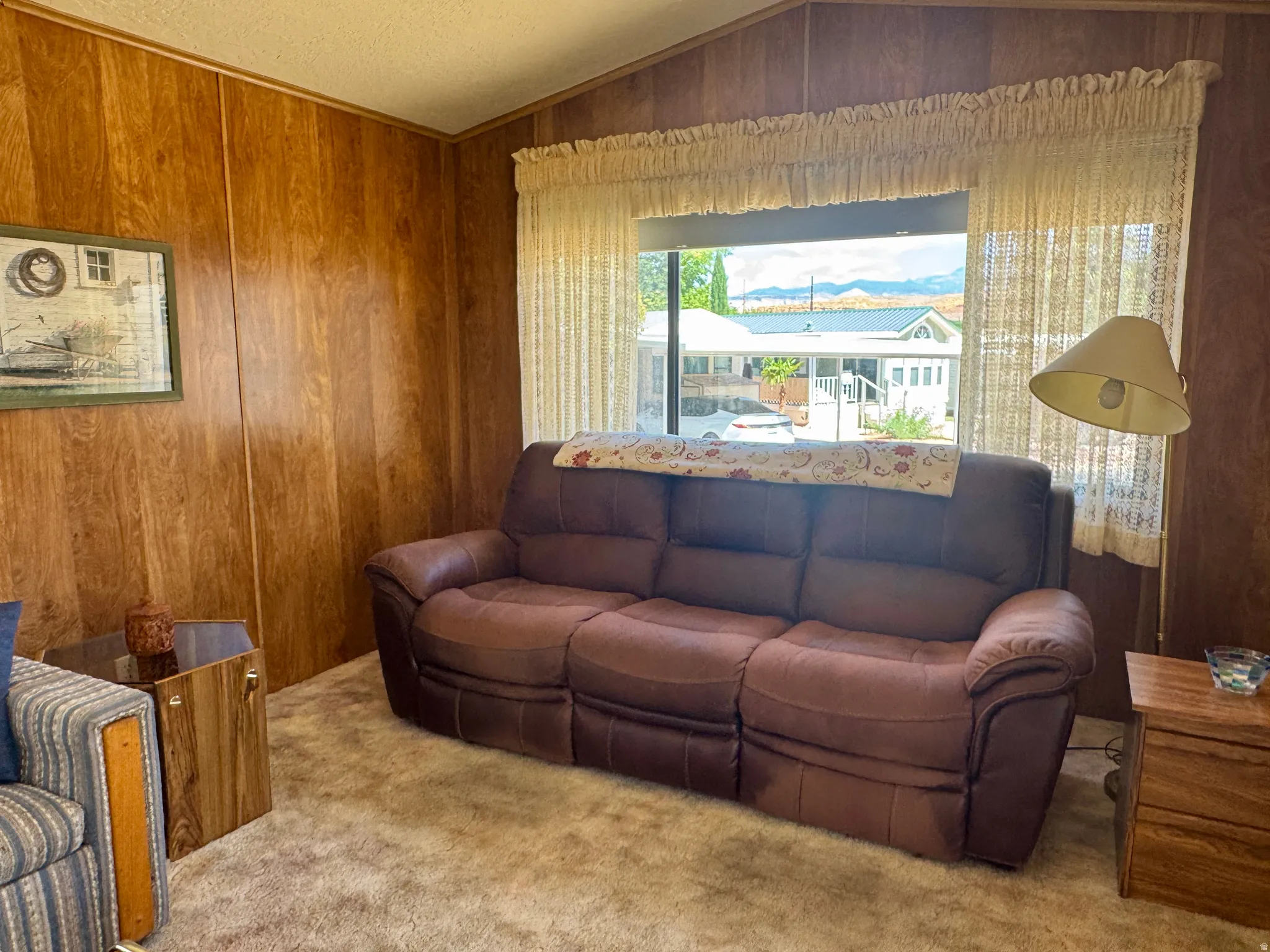 Carpeted interior space featuring wood-panel walls, a large window, and a sloped ceiling