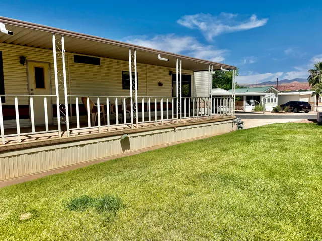Residential exterior featuring a covered porch with white railing, light-colored siding, and a manicured lawn