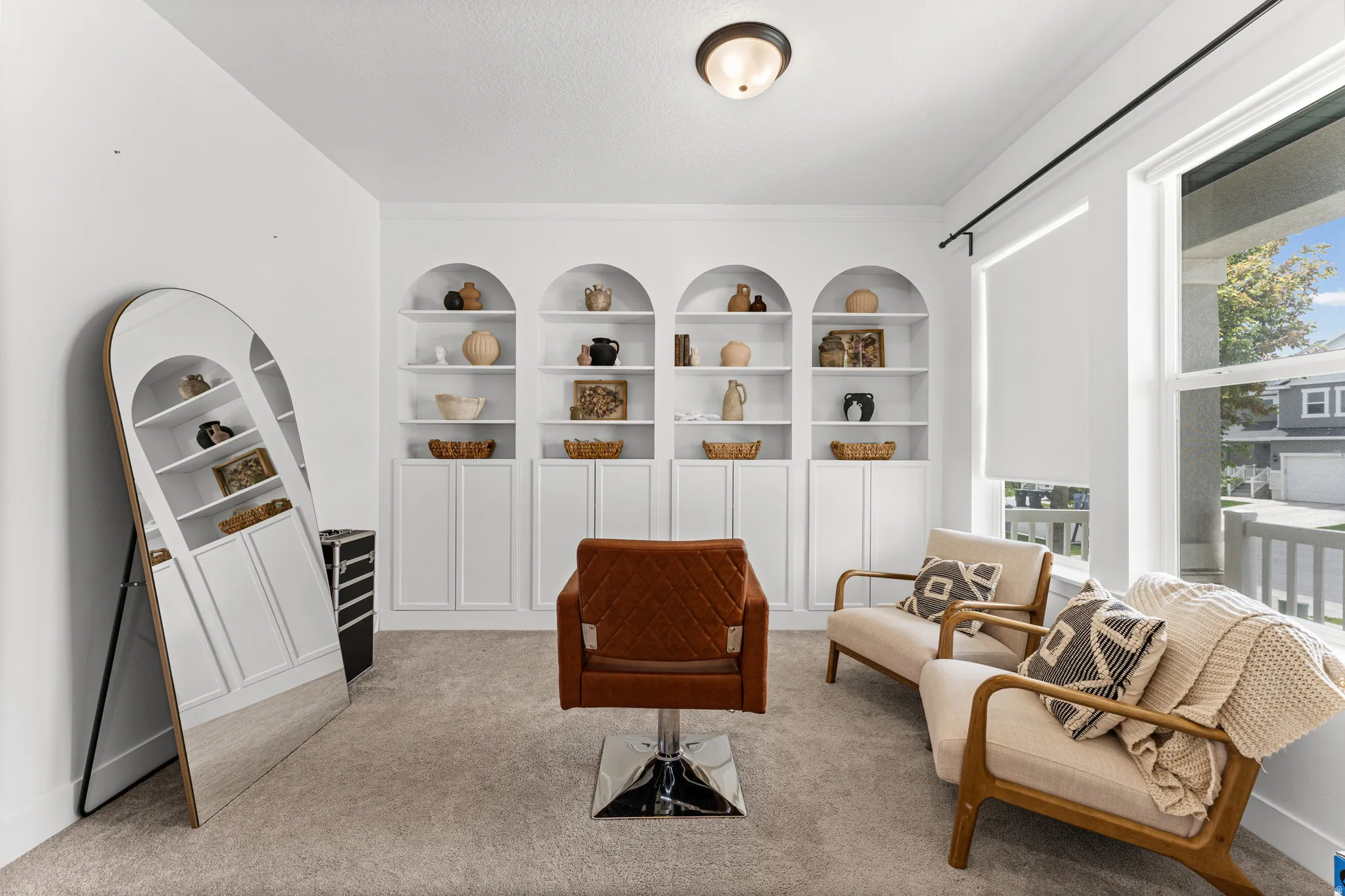 Built-in arched shelving with lower cabinetry, neutral wall-to-wall carpeting, and large windows with roller shades