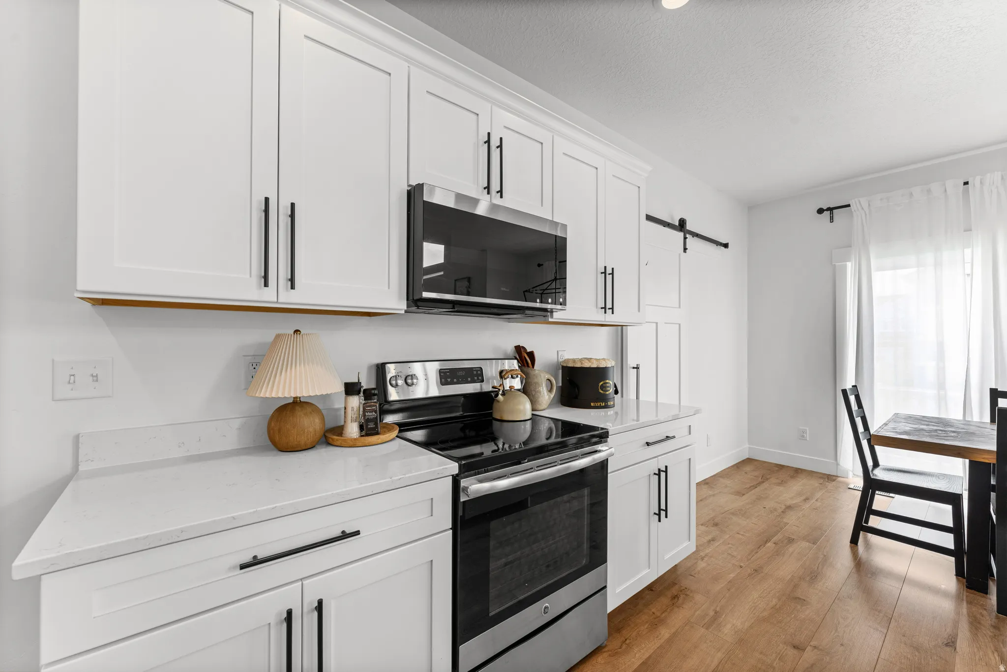Modern kitchen featuring white shaker cabinetry with matte black hardware, stone countertops, stainless steel appliances, and wood-finish flooring