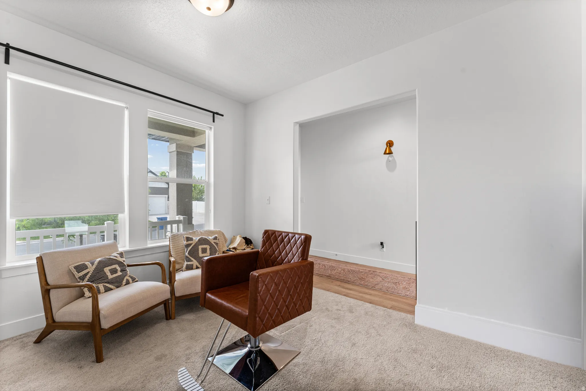 Carpeted interior space featuring two windows with roller shades, white trim, and a wide entryway to an additional room