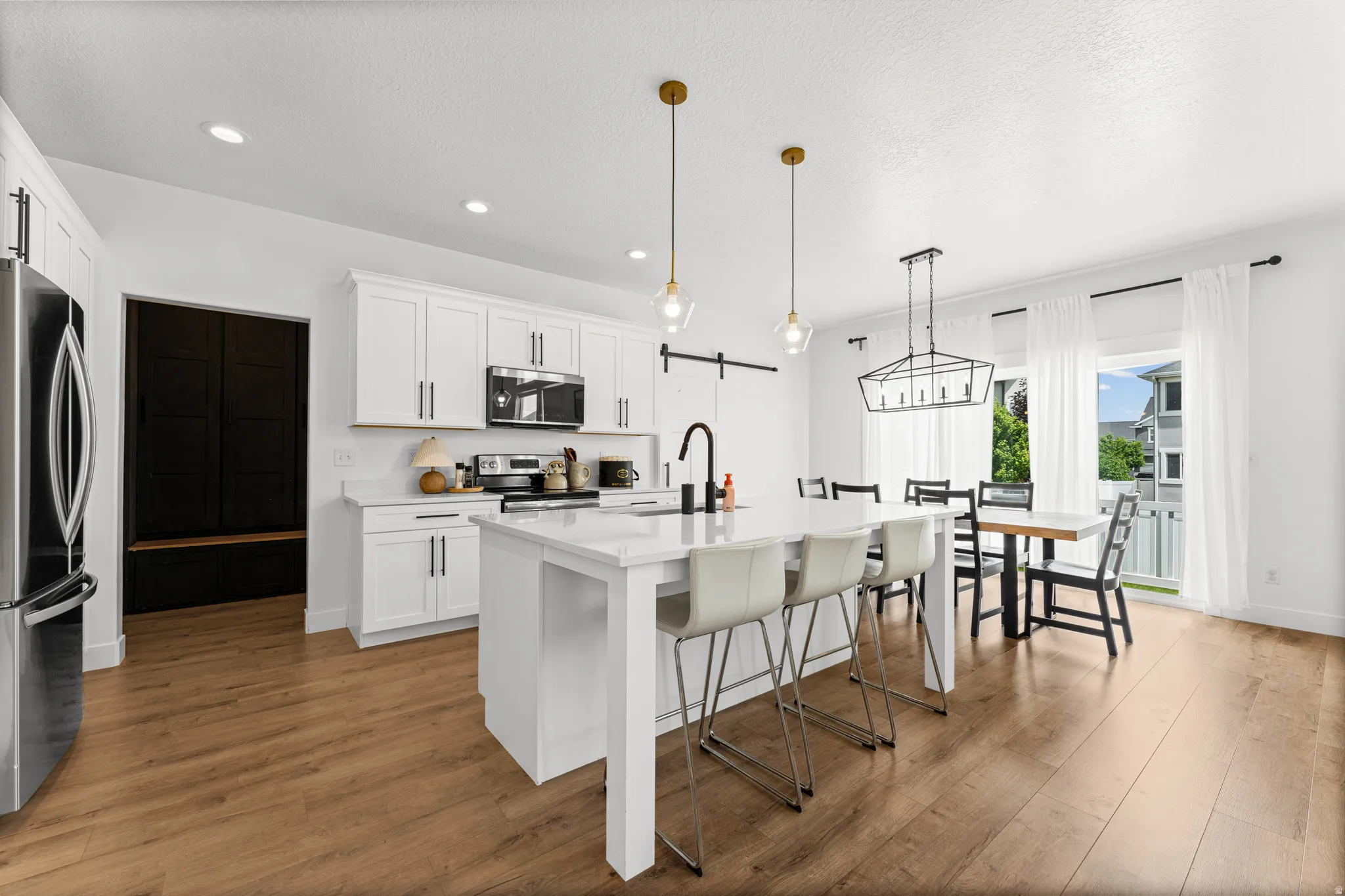 Modern kitchen featuring white cabinetry, stainless steel appliances, a center island with seating, wood-finish flooring, and a sliding glass door