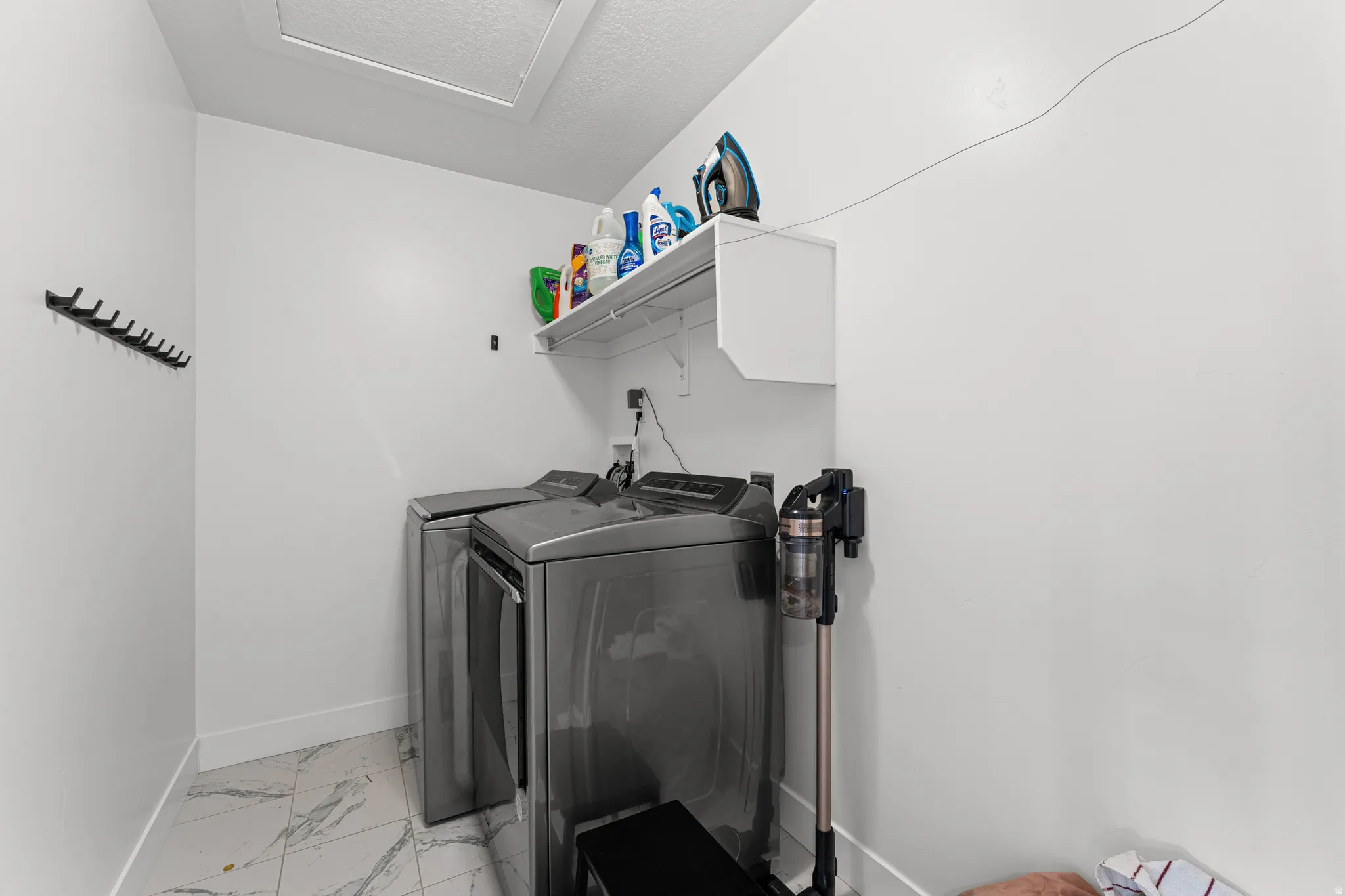 Dedicated utility space featuring marble-look tile flooring, white baseboards, and a white wall-mounted shelf