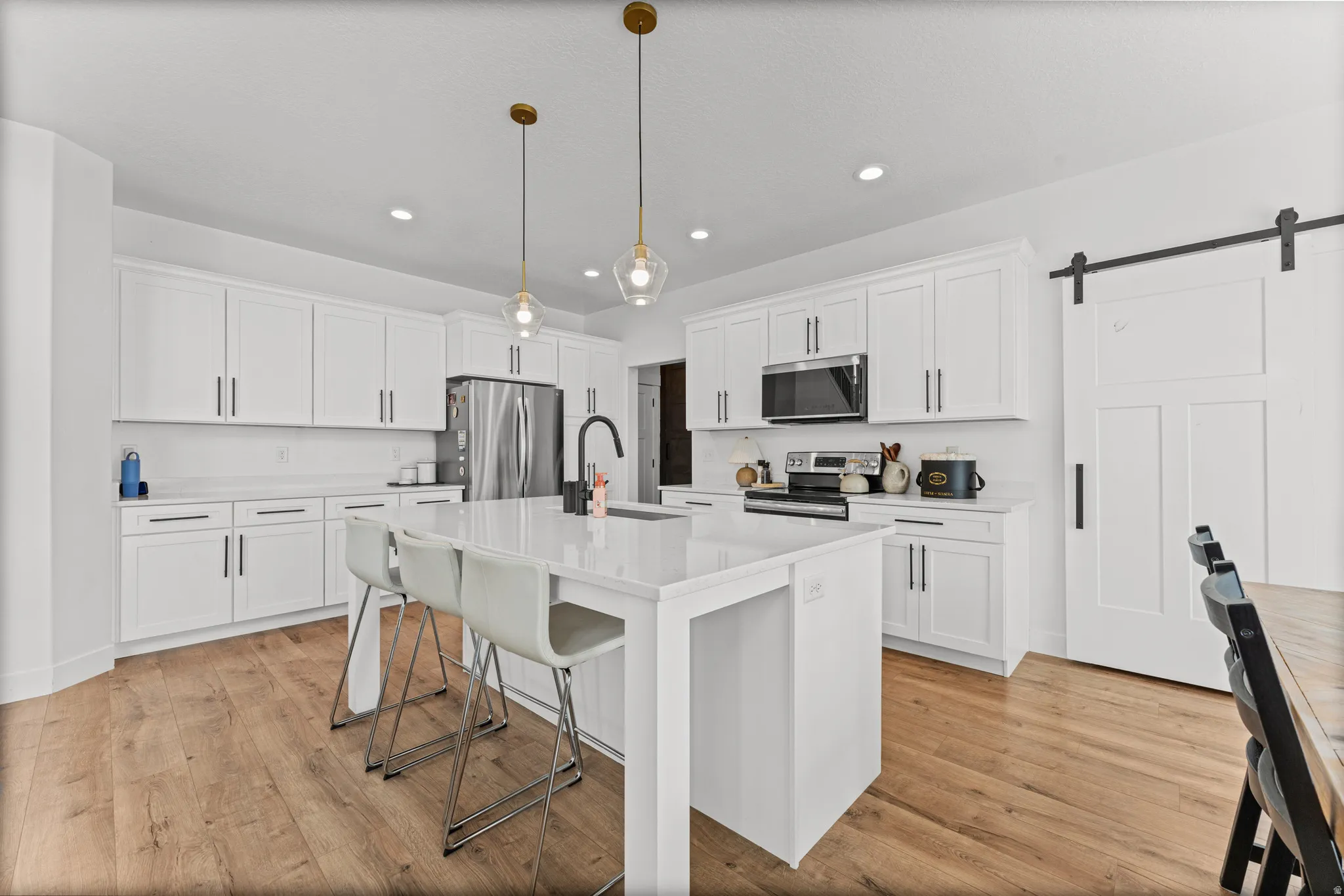 Modern kitchen featuring a large central island with seating, white shaker cabinetry, stainless steel appliances, and wood-finish flooring