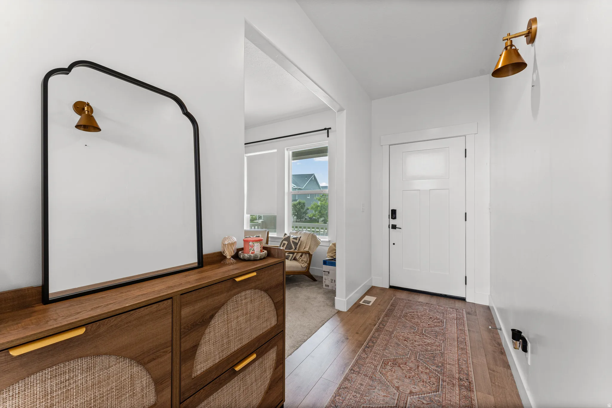 Bright entryway featuring wood-finish flooring, a white paneled entry door, and a decorative wall sconce