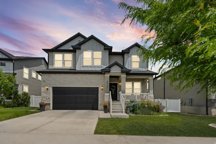 Modern two-story residence featuring a dark gray garage door, stacked stone accents, and a covered front porch with white railings