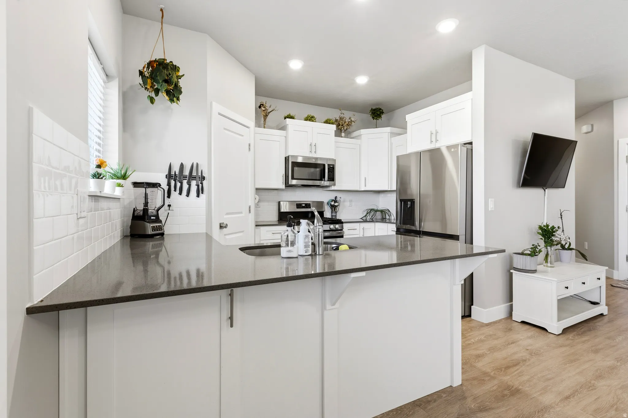 Spacious kitchen featuring an extended island with dark countertops, white cabinetry, stainless steel appliances, and a subway tile backsplash