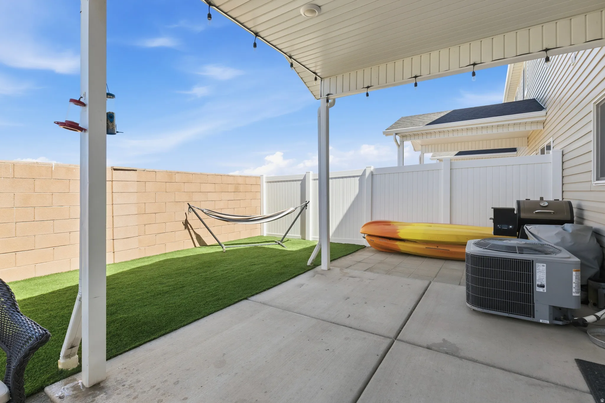 Covered patio with concrete flooring, featuring an artificial turf area and a block wall perimeter