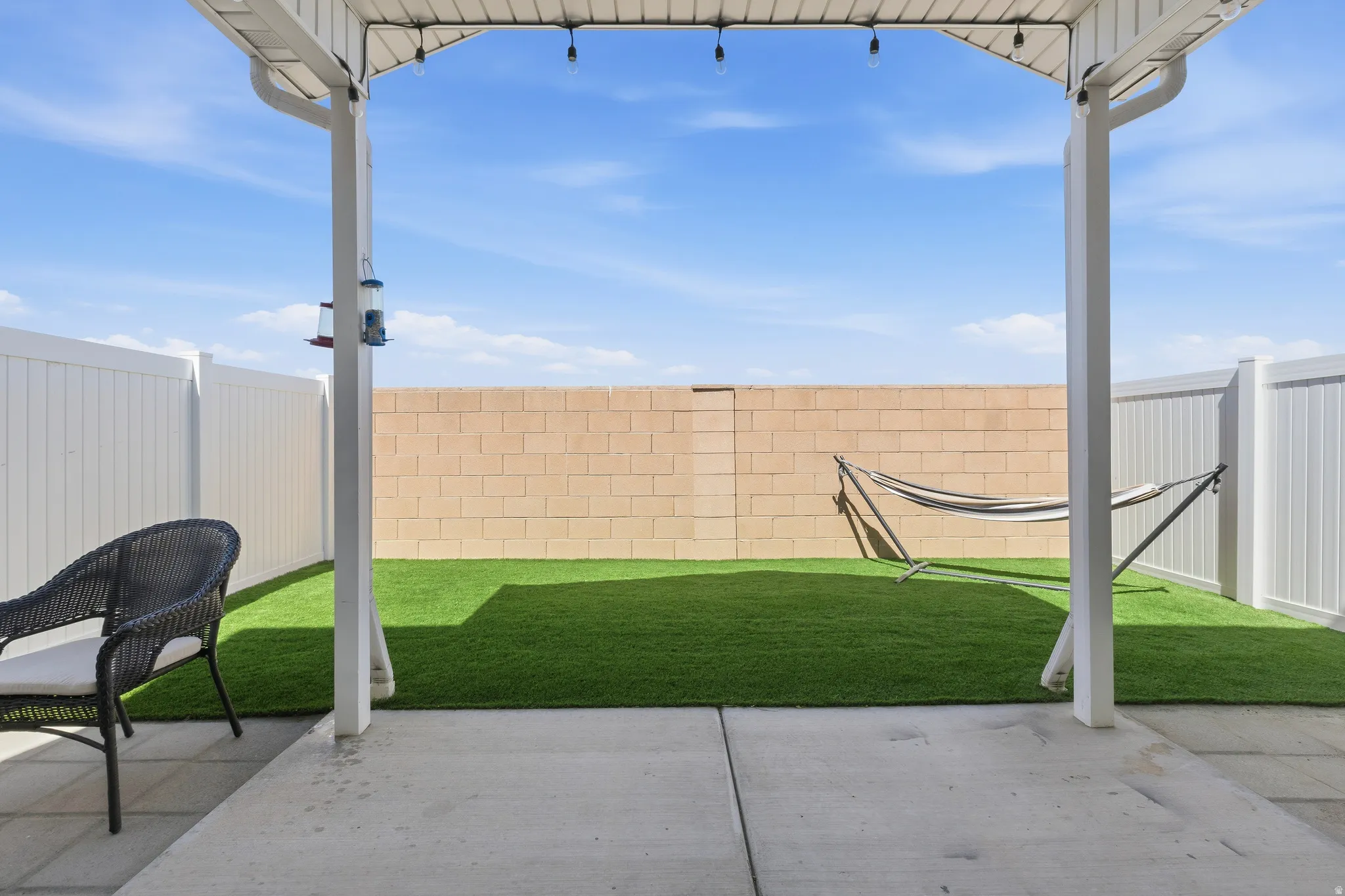 Covered concrete patio extending to a fenced backyard featuring artificial turf