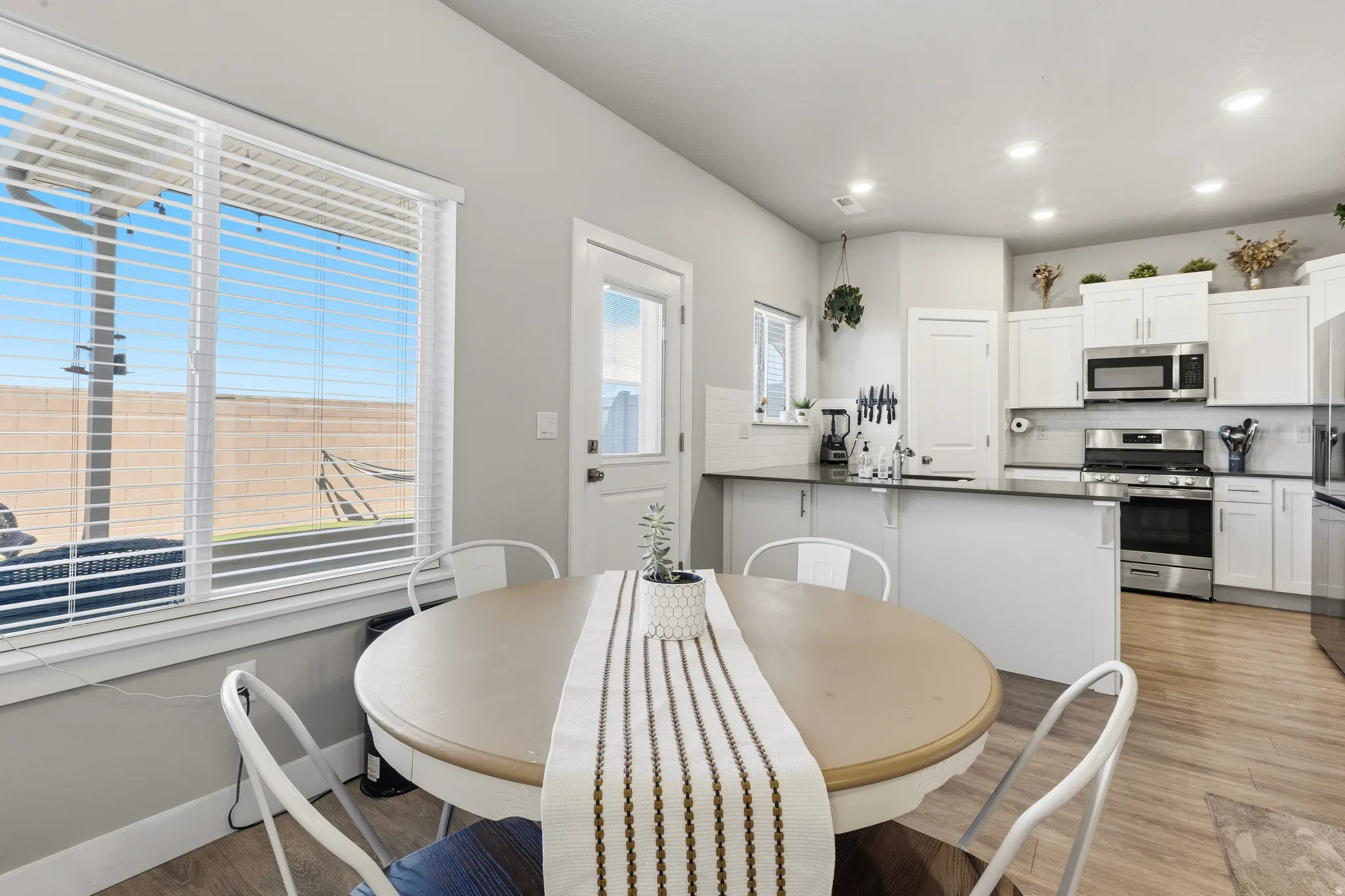 Bright kitchen and dining area featuring white cabinetry, stainless steel appliances, dark countertops, and wood-finish flooring