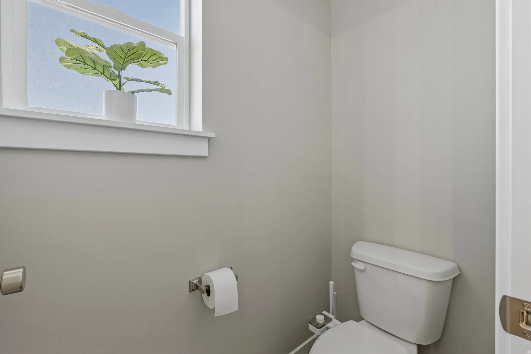 Bathroom featuring a single window with white trim, light gray walls, and a white toilet