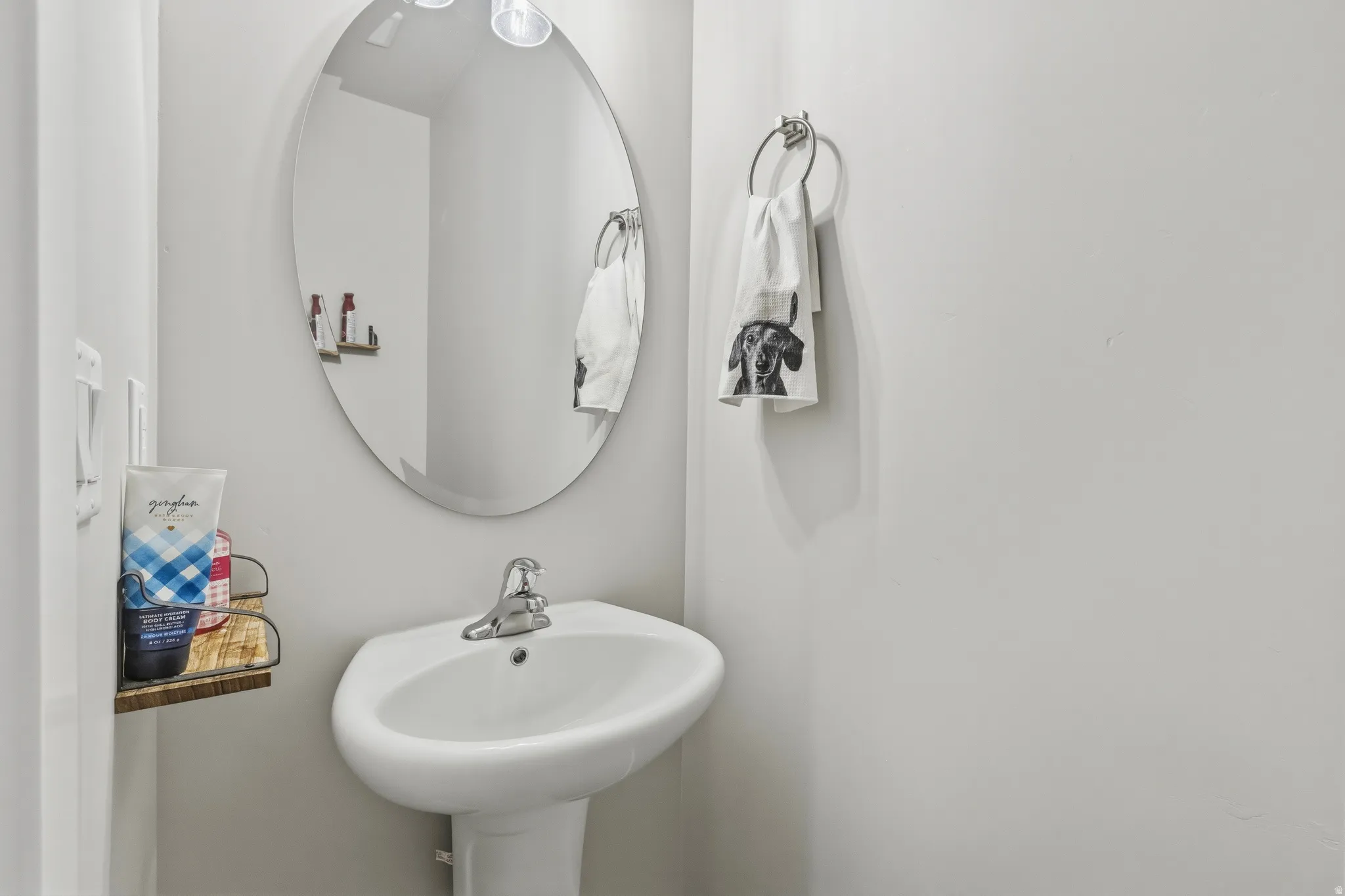 Pedestal sink with chrome faucet, complemented by an oval wall-mounted mirror