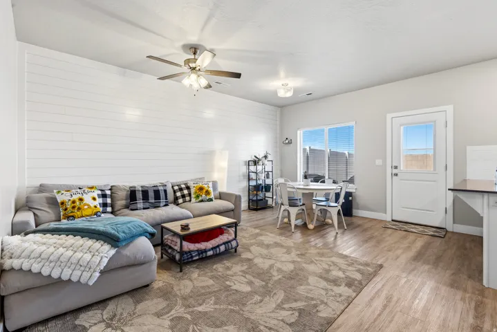 Open-concept living space featuring a shiplap accent wall, wood-finish flooring, a ceiling fan with integrated lighting, and a dining area with direct outdoor access