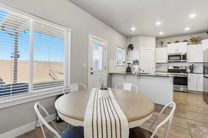 Bright kitchen and dining area featuring white cabinetry, stainless steel appliances, dark countertops, and wood-finish flooring