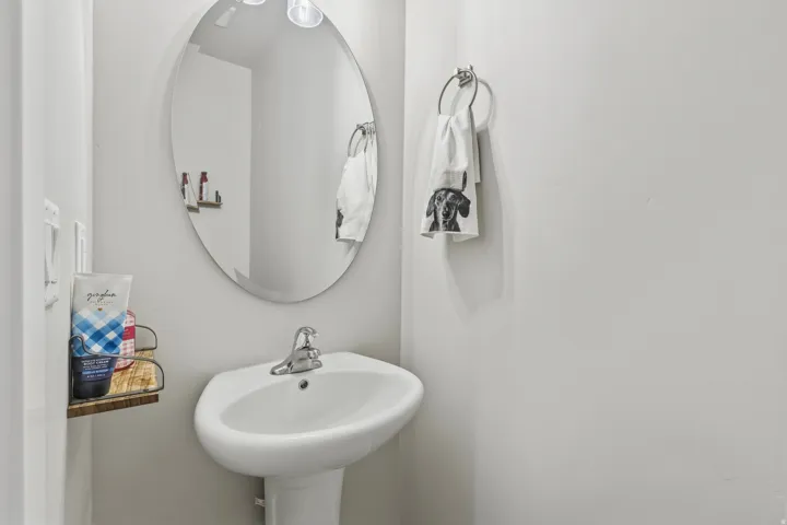 Pedestal sink with chrome faucet, complemented by an oval wall-mounted mirror