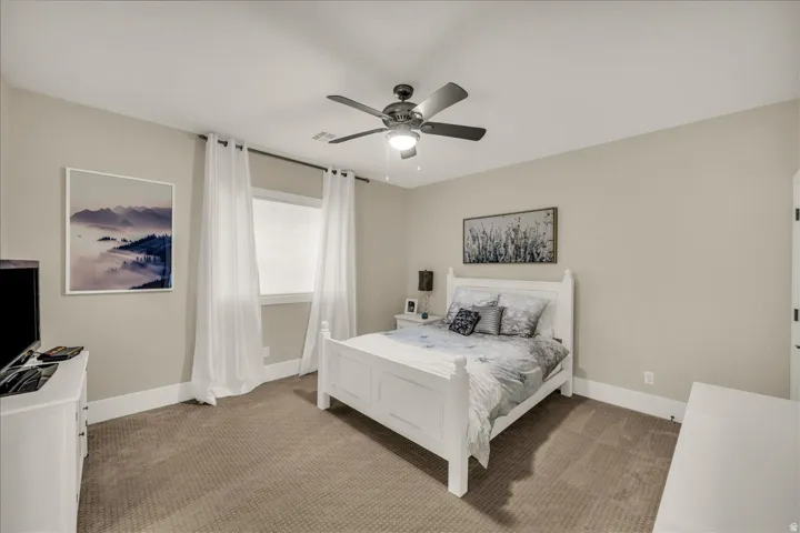 Spacious room featuring neutral-toned walls, plush carpeting, a large window, a ceiling fan with integrated lighting, and white baseboards