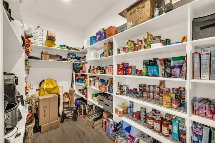 Spacious walk-in pantry featuring extensive white shelving, wood-finish flooring, and ample storage capacity