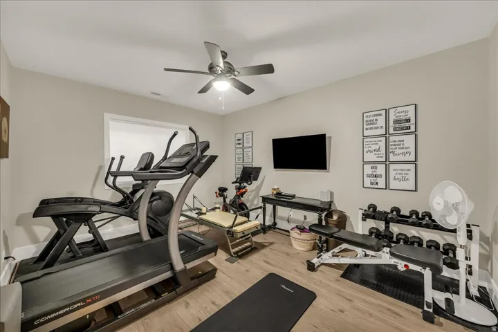 Dedicated fitness space featuring wood-finish flooring, neutral wall tones, a ceiling fan with integrated lighting, and a white-trimmed window