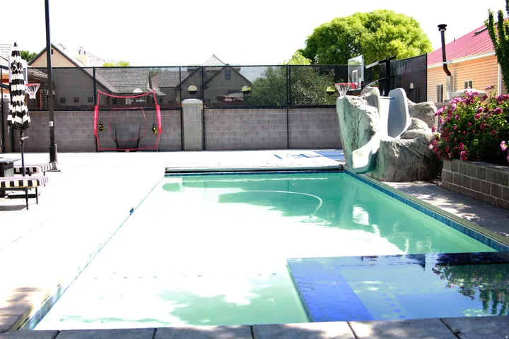 Swimming pool with concrete decking, integrated rock-feature slide, and block privacy wall