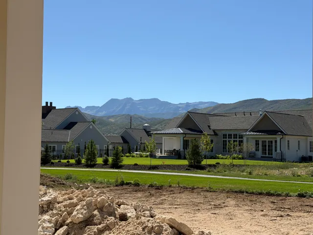Manicured lawn with mature landscaping, surrounded by residences featuring gabled roofs and a mountain backdrop