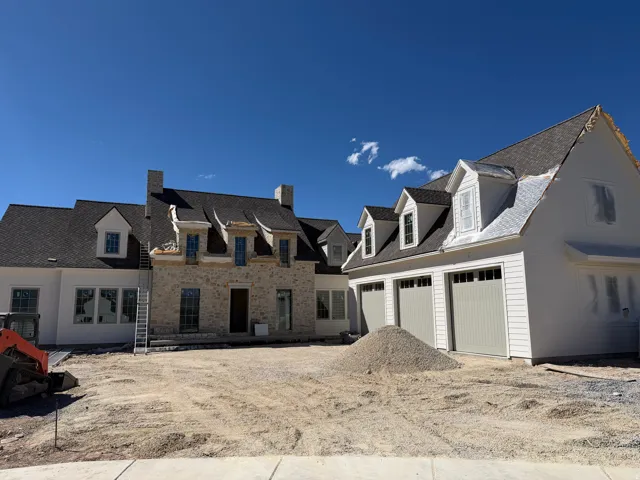Stone and siding exterior with multiple dormer windows, dark shingle roofing, and three paneled garage doors