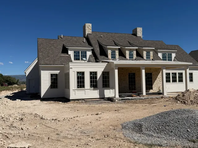 Stone and siding exterior with multiple dormer windows, a covered patio, and an attached two-car garage