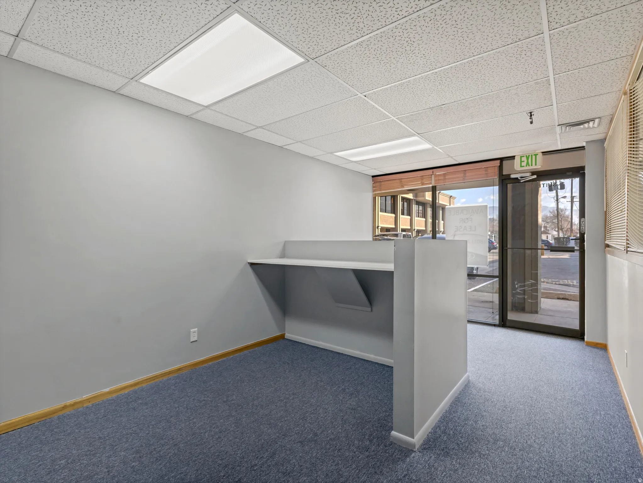 Open space featuring a built-in counter, blue carpeting, and a drop ceiling with integrated lighting