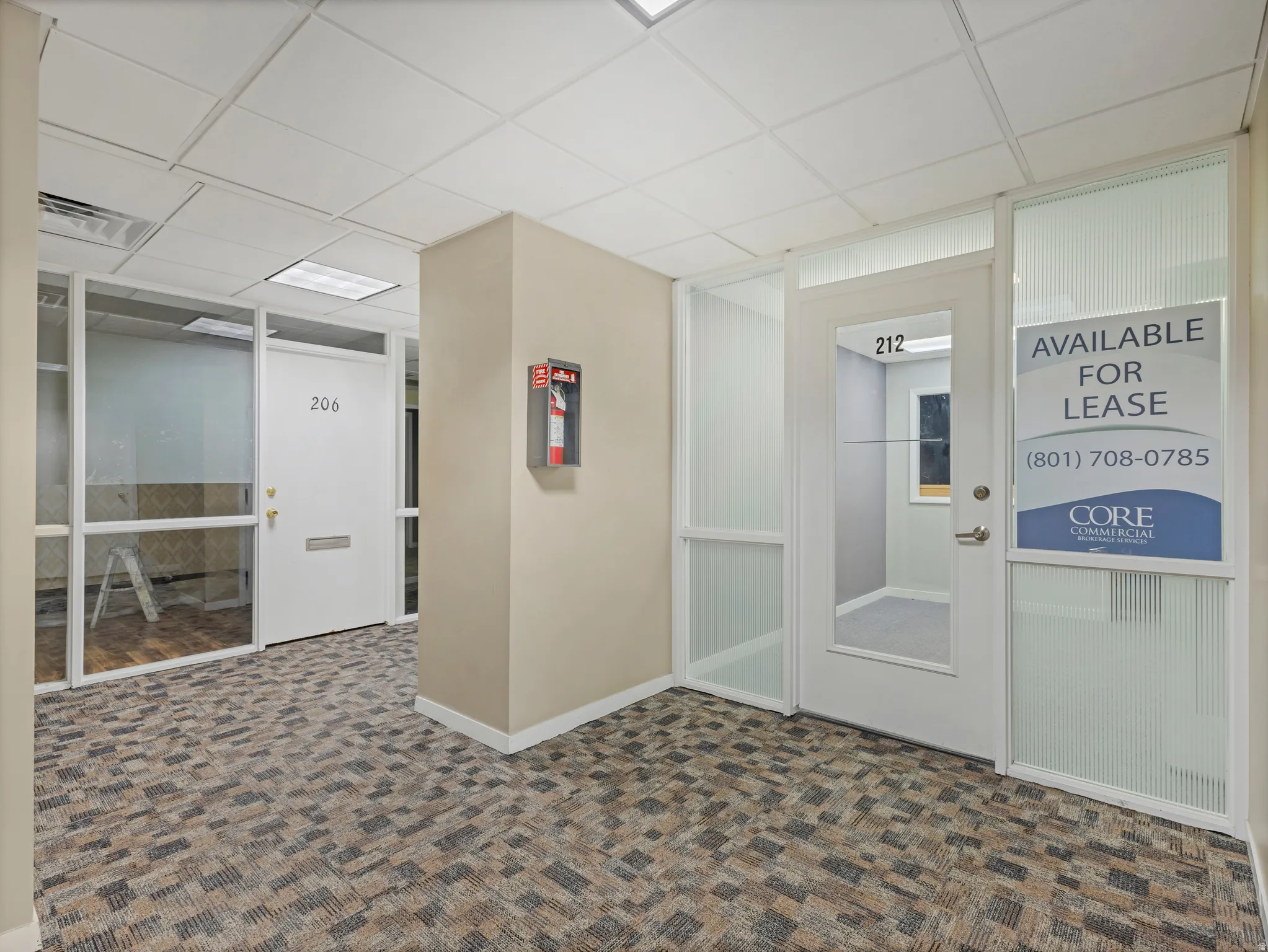 Commercial hallway with patterned carpet flooring, neutral-toned walls, and white baseboards