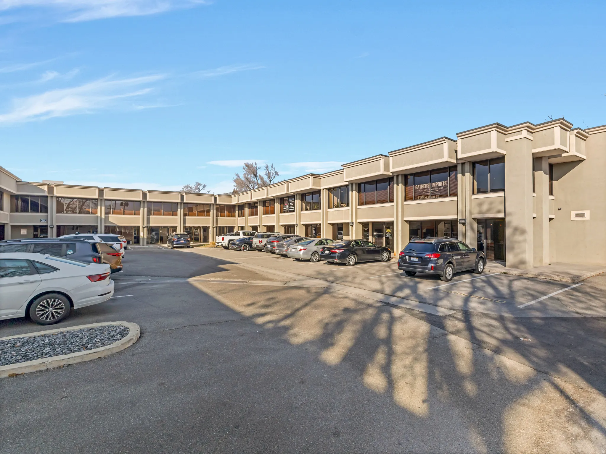 Commercial building featuring multiple storefronts, extensive surface parking, and a stucco exterior with decorative trim
