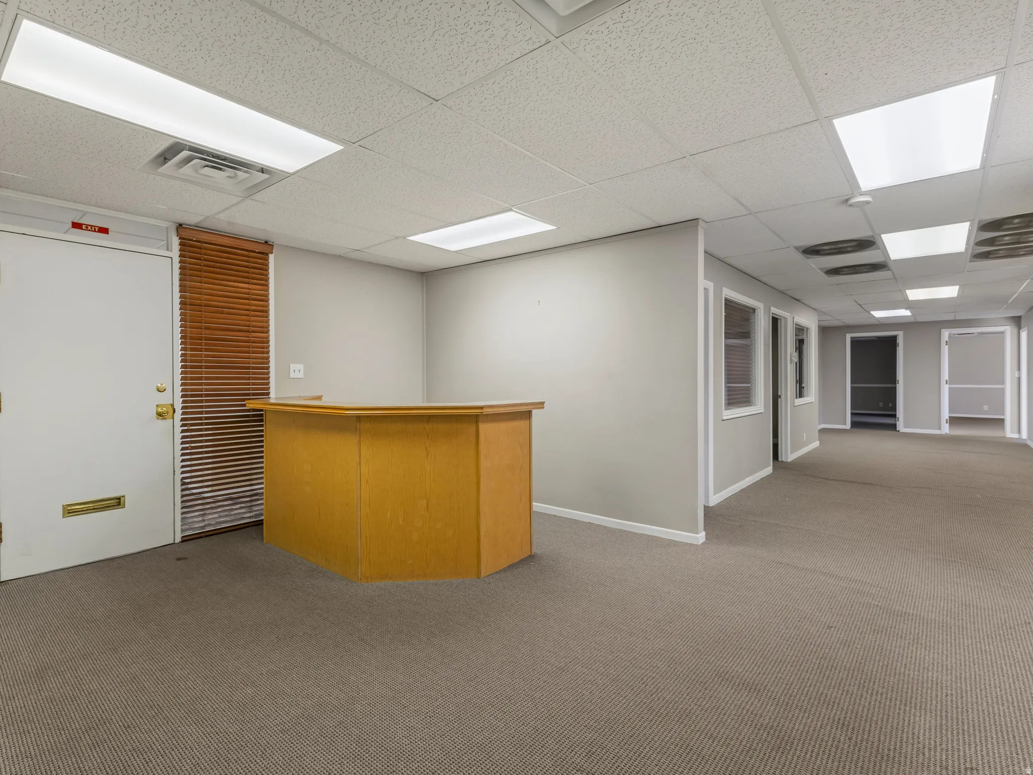 Reception area featuring a built-in wood-finish desk, textured carpet flooring, and a white drop ceiling with recessed lighting
