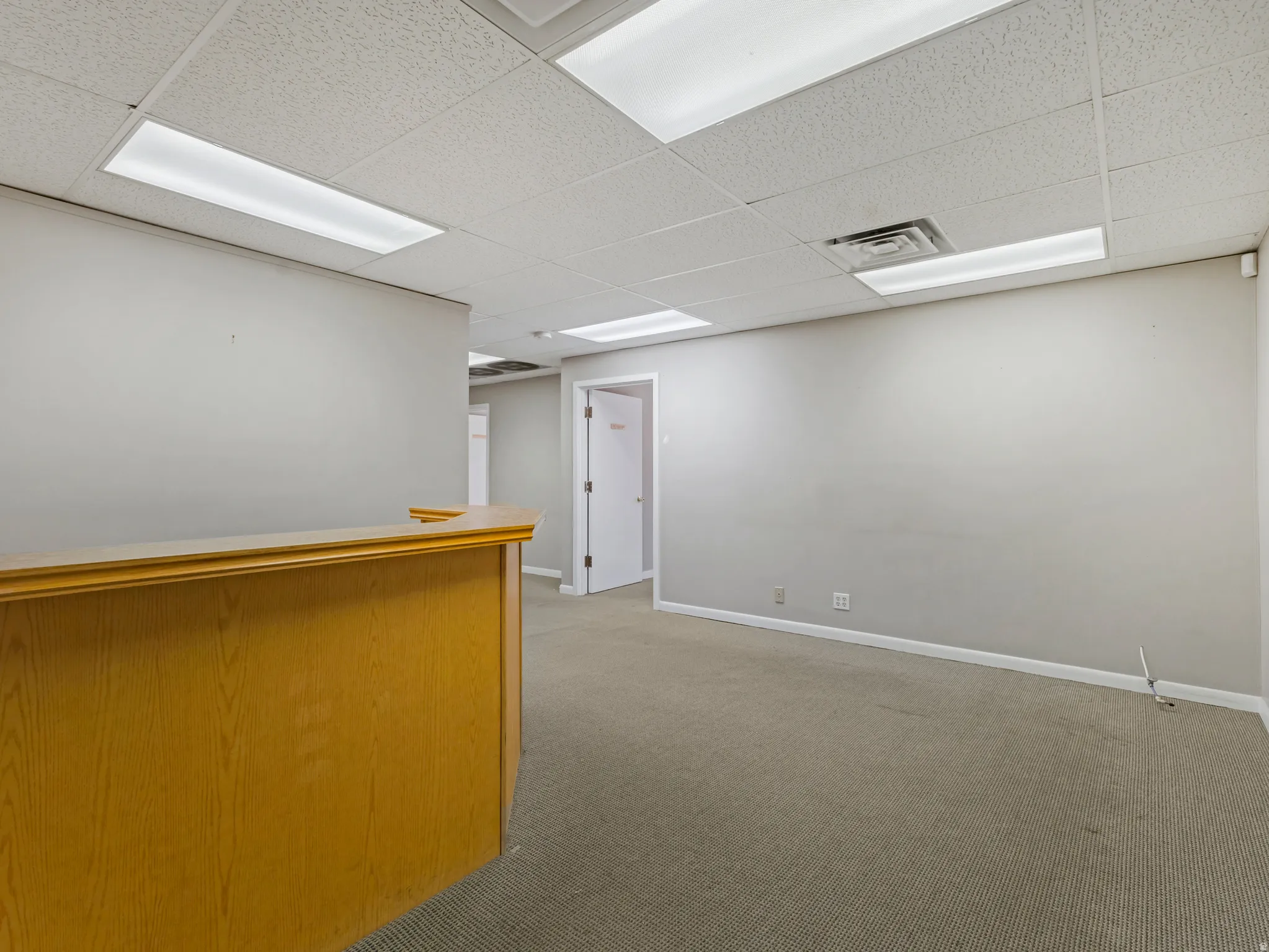 Wood-tone reception counter with neutral gray walls and carpeted flooring
