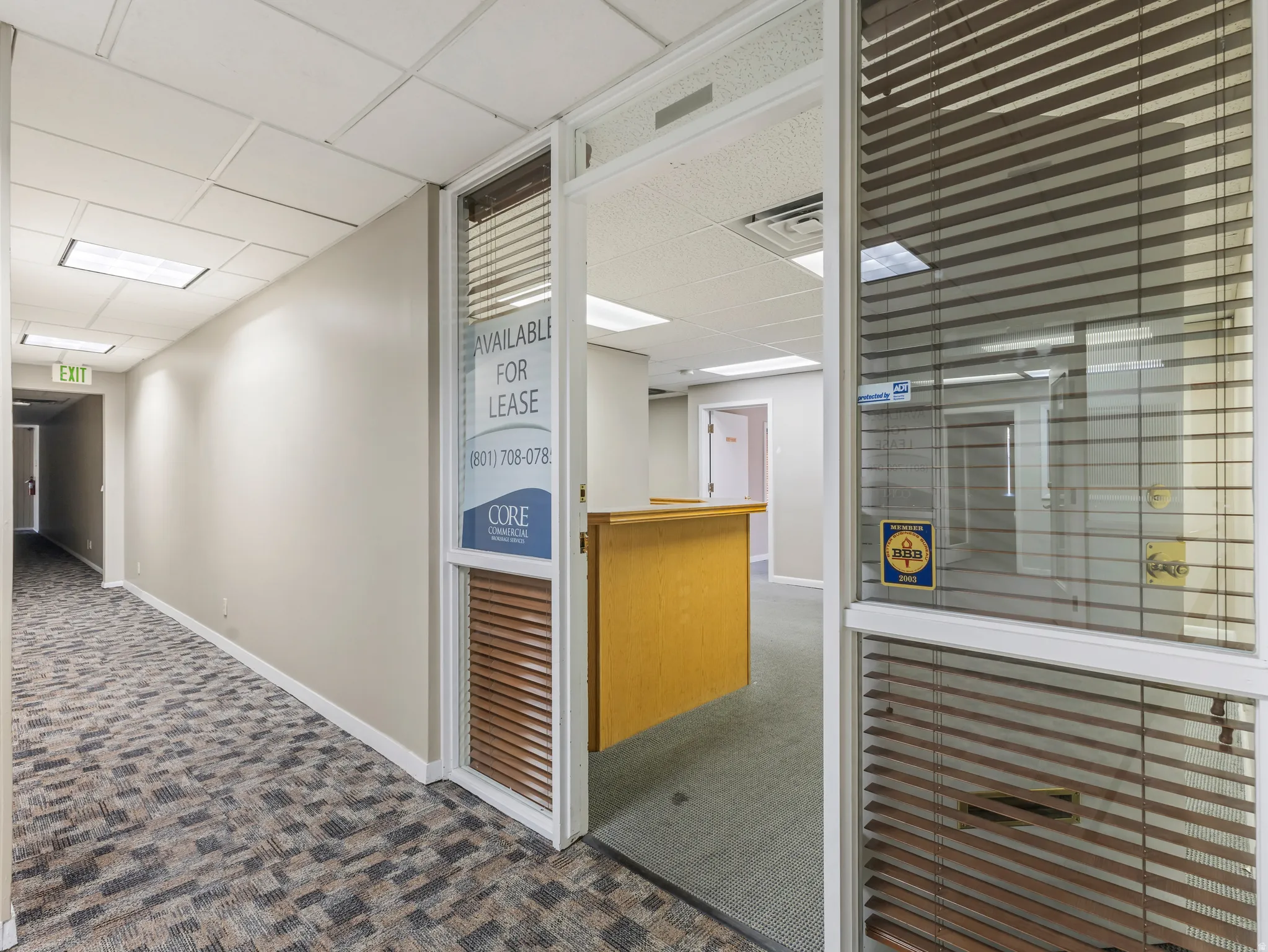 Commercial office space featuring a glass entrance door with blinds, textured carpet flooring, and recessed ceiling lighting