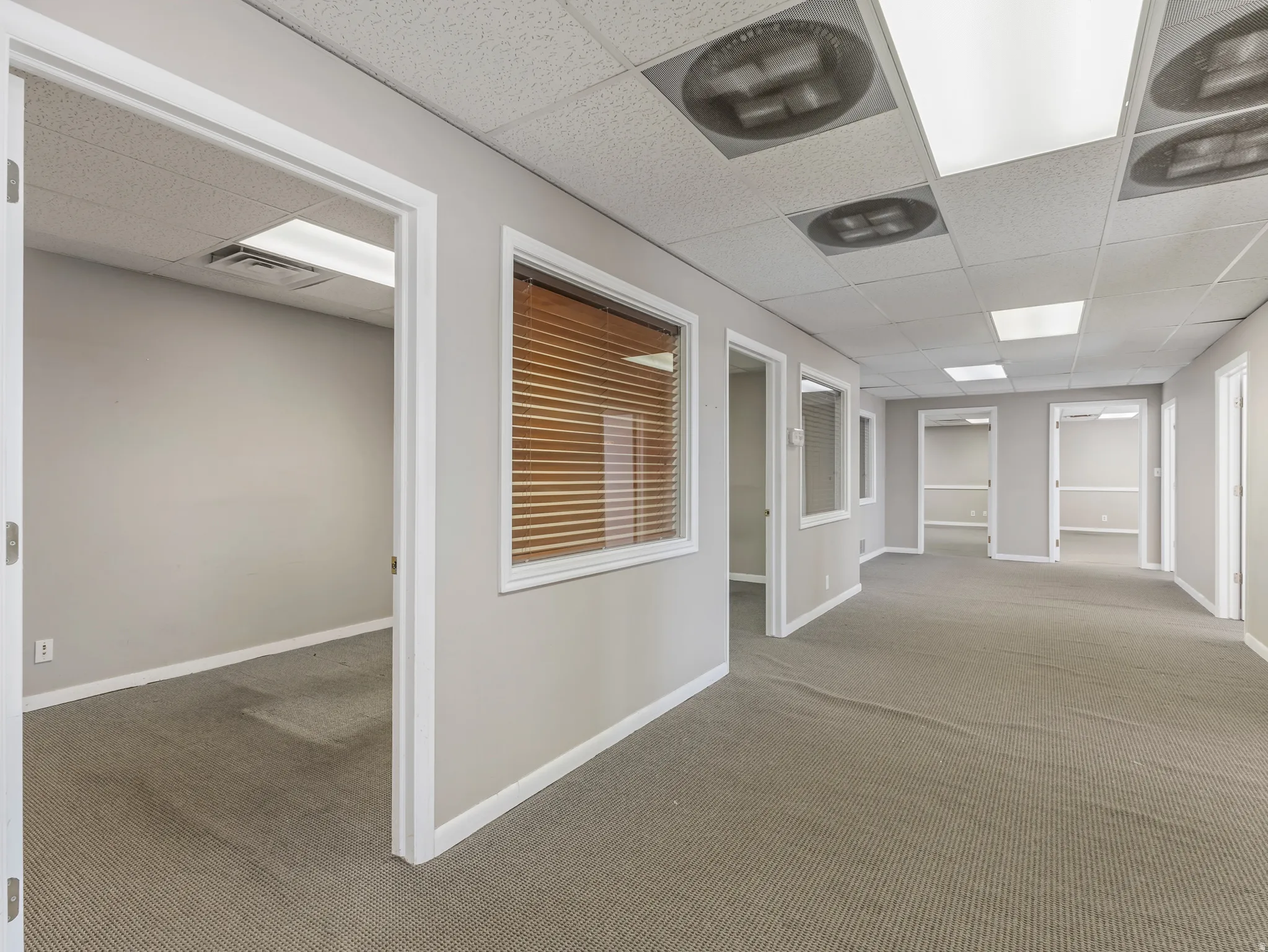 Spacious commercial corridor featuring neutral gray walls and patterned carpet flooring