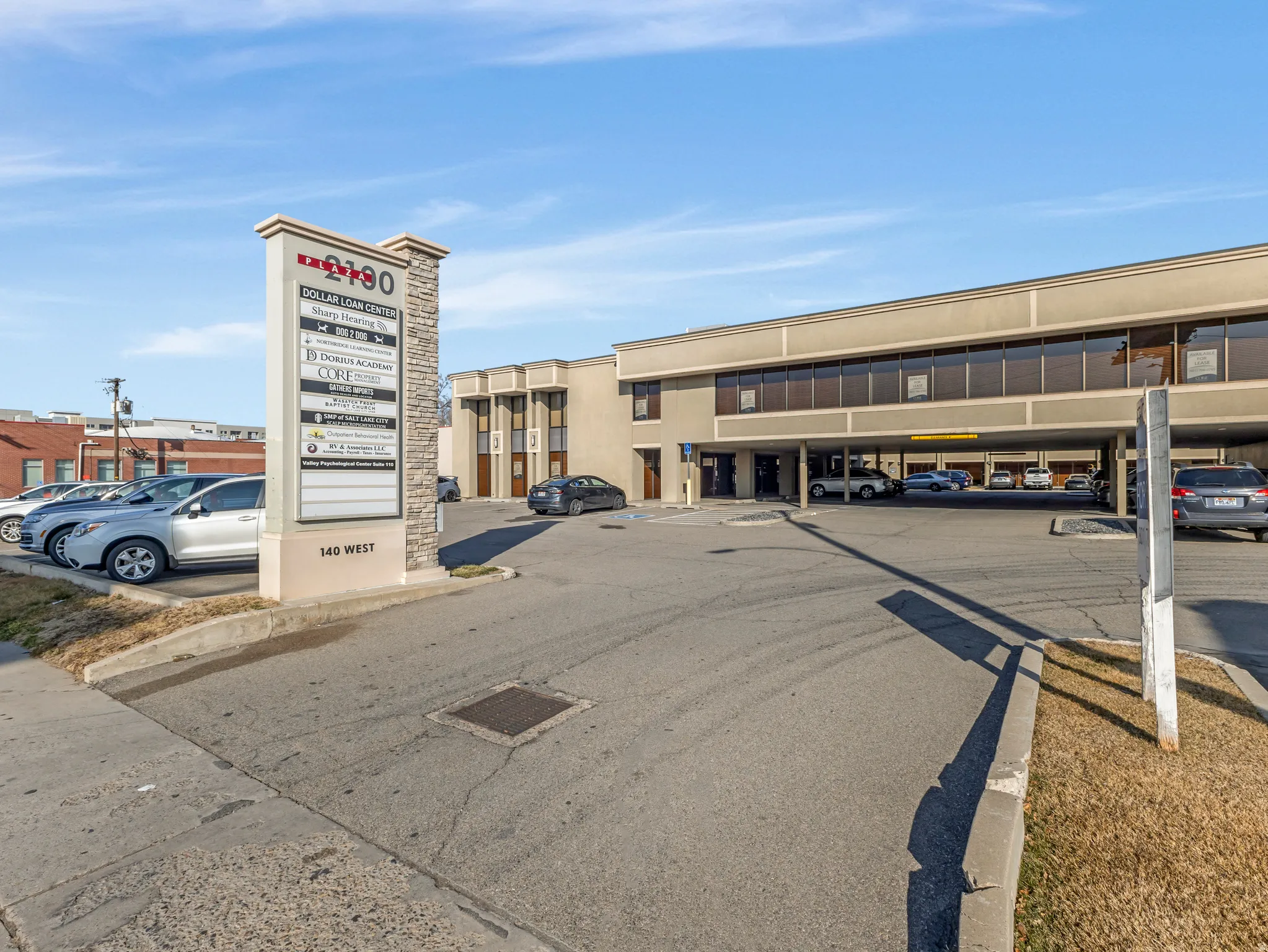 Commercial building featuring a stone and stucco monument sign, a paved parking area, and an integrated covered parking structure